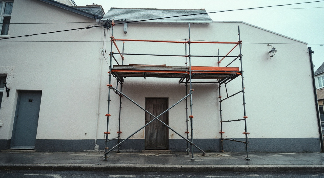 Échafaudage en cours de montage devant une façade enduite, avec un câble électrique aérien protégé par des gaines isolantes orange au-dessus du dernier plancher.